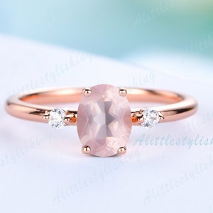 May include: A rose gold ring with a large oval pink gemstone and two smaller round clear gemstones on the band.