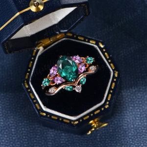 May include: A rose gold ring set with a large emerald green pear-shaped stone surrounded by smaller pink and green stones. The ring is in a blue velvet ring box.