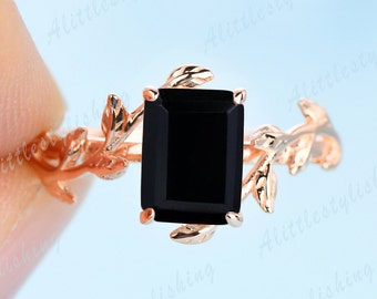 Könnte beinhalten: Ein Ring aus Roségold mit einem schwarzen, quadratischen Edelstein, der in einem zarten Blattdesign gefasst ist.