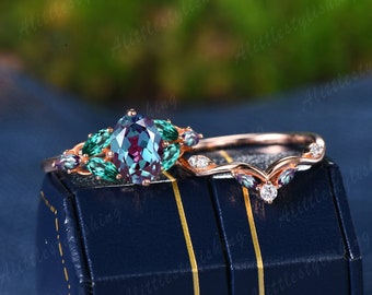May include: A rose gold engagement ring set with a large oval alexandrite gemstone surrounded by smaller green gemstones. The matching wedding band features a delicate vine design with smaller alexandrite gemstones.
