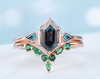 May include: A rose gold engagement ring set with a large octagon-shaped blue gemstone surrounded by smaller blue gemstones. The ring also features a delicate band with a row of emerald green gemstones.
