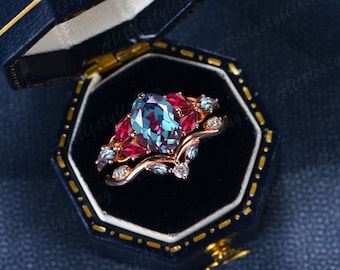 May include: A rose gold ring set with a large oval alexandrite gemstone surrounded by smaller red and blue gemstones. The ring is in a blue velvet ring box.