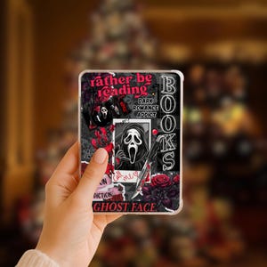 May include: A phone case featuring a collage design with the text "rather be reading" in pink. The design includes a black and white image of a Ghost Face mask, roses, and the words "Dark Romance Addict" and "Books".