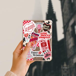May include: A clear phone case with various stickers. The stickers include phrases like "I'd Rather Be Reading," "Book Addict," and "One More Chapter." Other stickers feature playing cards, a pack of cigarettes, and the words "Busy Woman."
