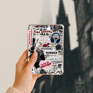 May include: A clear phone case with a collage of stickers featuring text like "In My Dark Romance Era" and "Romance with a side of Murder." The stickers include roses, a skull, and a heart-shaped graphic with the text "I'm here for Red Flags."