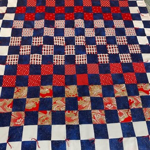 May include: A handmade quilt with a patchwork design. The quilt features a checkerboard pattern of navy blue, red, and white squares. Some squares have patterned fabric, including polka dots and paisley. Red ties secure the layers.