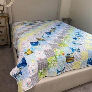 May include: A patchwork quilt with a variety of fabric patterns, including floral, plaid, and solid colors, covers a bed. The quilt features a mix of blues, greens, yellows, and whites. The bed has a neutral-colored headboard and base.