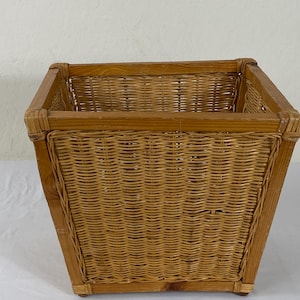 May include: A square-shaped basket constructed with a sturdy wooden frame and woven wicker panels on all four sides. The natural light brown wood and wicker material create a consistent texture throughout the open-top storage container.
