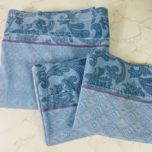 May include: Three light blue bed linens with a paisley and floral design. The top portion of each linen features a dark blue paisley pattern, separated by a thin purple stripe from the light blue geometric patterned bottom.