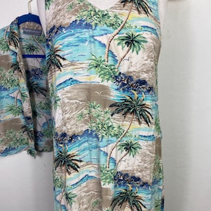 May include: A sleeveless dress and matching button-down shirt featuring a tropical print with palm trees, ocean waves, and a beach scene. The dress has a V-neck and is displayed on a mannequin. The shirt is on a hanger.