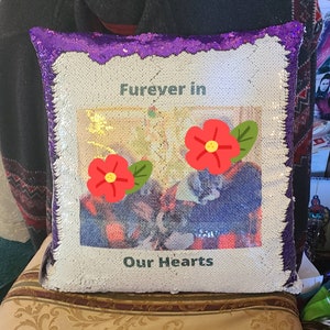May include: A reversible sequin pillow with a white and purple border. The pillow features the text "Furever in Our Hearts" with two red flower graphics. The center of the pillow has a photo of a pet.