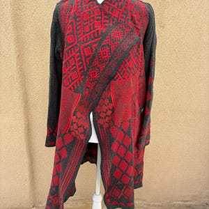 Puede incluir: Un c&aacute;rdigan largo y abierto en gris y rojo, exhibido en un maniqu&iacute; blanco. El c&aacute;rdigan presenta un patr&oacute;n geom&eacute;trico en rojo sobre un fondo gris. Las mangas son grises lisas.