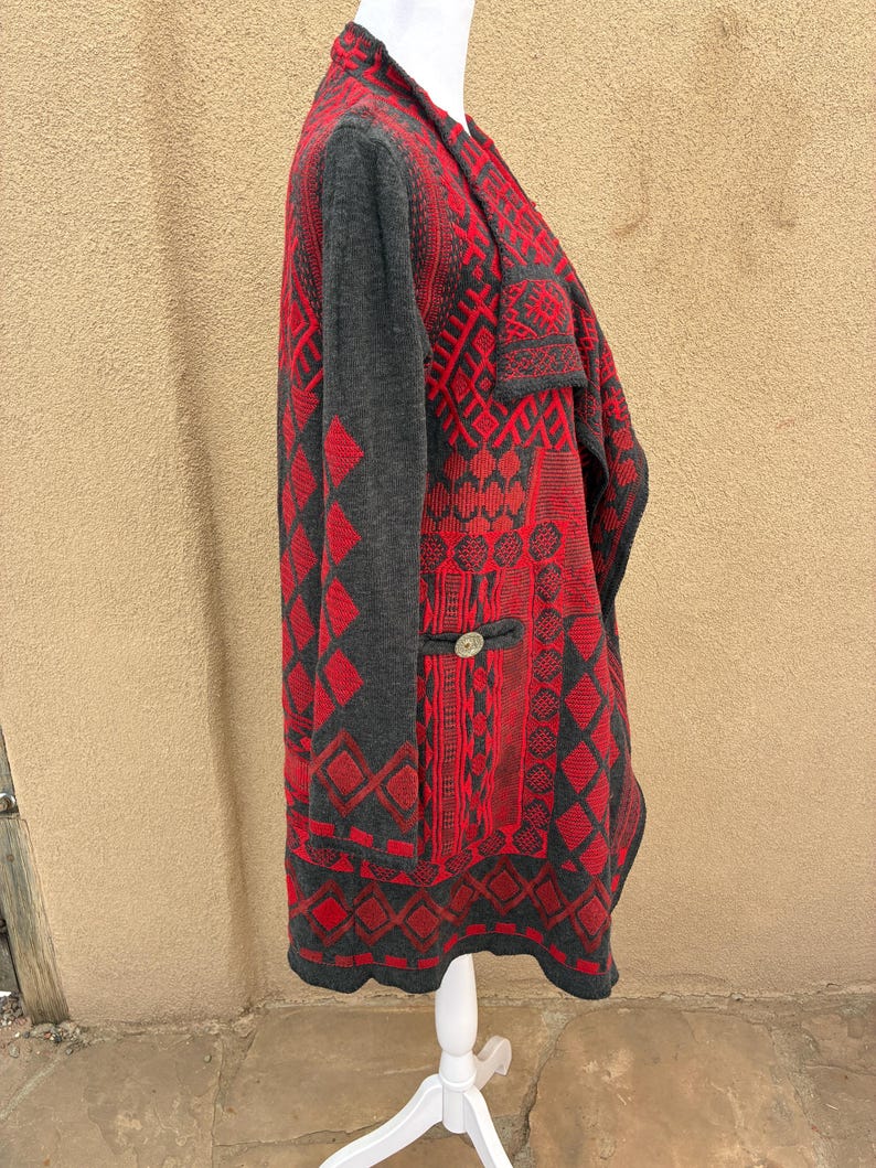 Puede incluir: Un c&aacute;rdigan estampado en rojo y gris con un dise&ntilde;o geom&eacute;trico. El su&eacute;ter de manga larga presenta un cierre de bot&oacute;n y un cuello chal. El c&aacute;rdigan se exhibe en un maniqu&iacute; blanco.