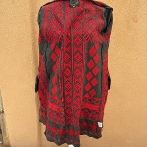 Puede incluir: Un abrigo estampado en gris y rojo exhibido en un maniqu&iacute; blanco. El abrigo presenta un dise&ntilde;o geom&eacute;trico en rojo sobre un fondo gris. El abrigo tiene cuello y bolsillos.