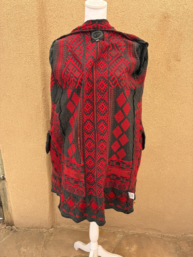 Puede incluir: Un abrigo estampado en gris y rojo exhibido en un maniqu&iacute; blanco. El abrigo presenta un dise&ntilde;o geom&eacute;trico en rojo sobre un fondo gris. El abrigo tiene cuello y bolsillos.