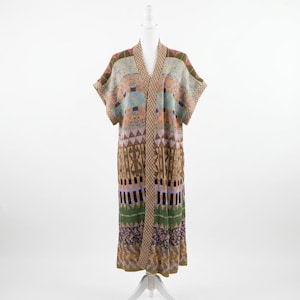 May include: A long, patterned cardigan in shades of brown, green, purple, and blue. The open-front garment features a V-neck and short sleeves. The design includes geometric and abstract patterns, displayed on a white mannequin.
