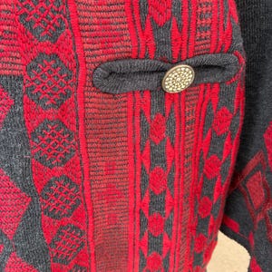 Puede incluir: Primer plano de una chaqueta estampada roja y gris. La chaqueta presenta intrincados dise&ntilde;os bordados en rojo sobre un fondo gris. Se ve un peque&ntilde;o bolsillo con un bot&oacute;n decorativo.
