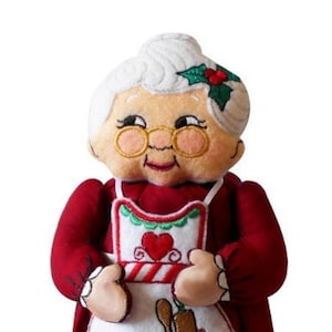 May include: A plush Christmas doll of a woman wearing a red dress and a white apron with a candy cane and heart design. She has white hair and a friendly face.