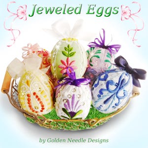 May include: Six intricately embroidered Easter eggs in a woven basket. The eggs are decorated with floral and geometric patterns, beads, and rhinestones. The eggs are in shades of green, blue, white, and yellow. The title "Jeweled Eggs" and the text "by Golden Needle Designs" are visible below the basket.