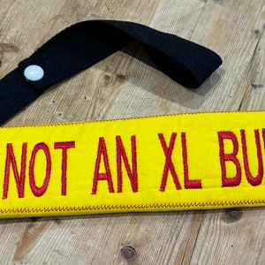 May include: Yellow fabric dog collar with a black strap and a white button. The collar has red embroidered text that reads "I AM NOT AN XL BULLY".