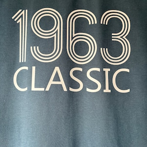 Könnte beinhalten: Ein dunkelblaues T-Shirt mit weißem Text, der "1963 CLASSIC" lautet.