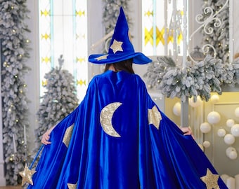 Könnte beinhalten: Ein blauer Samtmantel mit goldenen Glitzersternen und einem Halbmond. Der Umhang hat eine spitze Kapuze und ist perfekt für ein Zauberer-Kostüm.