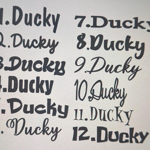 May include: A collection of twelve "Ducky" text designs in various fonts and styles. The text is in black, with each design numbered from 1 to 12. The background is a light, neutral color.