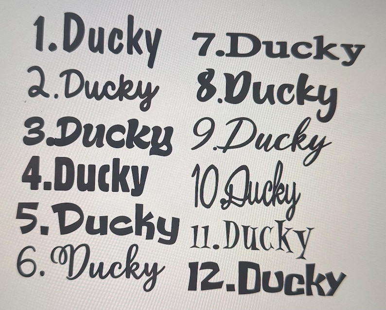 May include: A collection of twelve "Ducky" text designs in various fonts and styles. The text is in black, with each design numbered from 1 to 12. The background is a light, neutral color.