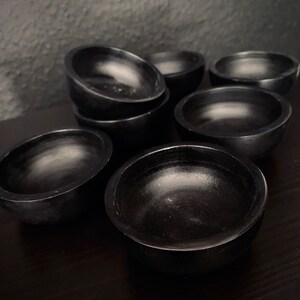 May include: A set of eight black, round, wooden bowls. The bowls are all the same size and shape, and they are arranged in a staggered pattern.