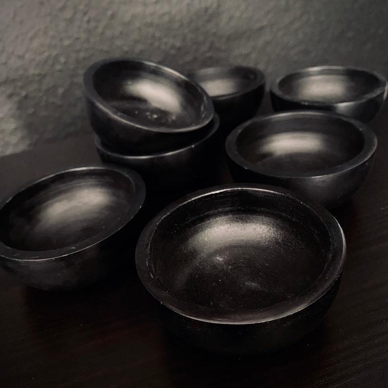 May include: A set of eight black, round, wooden bowls. The bowls are all the same size and shape, and they are arranged in a staggered pattern.