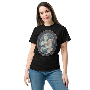 May include: Black t-shirt featuring an oval graphic of a woman holding a piglet, with text around the border. The text reads "HASTA QUE LA ULTIMA JAULA QUEDE VACIA". The shirt is made of a soft material.