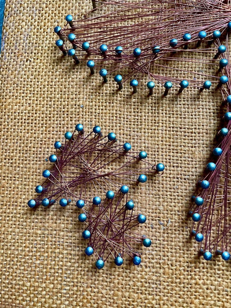 Pode incluir: Um close-up de uma pe&ccedil;a de arte de cordas com contas azuis e fio de cobre. A arte est&aacute; em um fundo de juta.