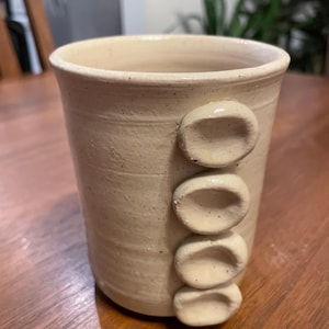 May include: A white ceramic vase with a textured surface and three raised circles on the side.