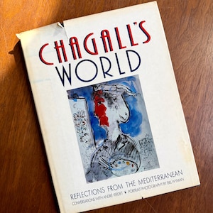 May include: A book titled "CHAGALL'S WORLD" with red and blue lettering. The cover features a colorful illustration of a person with a red face and a palette. The text "REFLECTIONS FROM THE MEDITERRANEAN" is also visible.