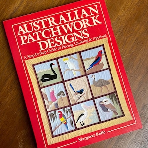 May include: A red book titled "Australian Patchwork Designs" with a step-by-step guide to piecing, quilting, and appliqué. The cover features a patchwork design with various Australian birds. The author's name, Margaret Rolfe, is at the bottom.