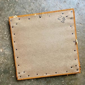 Pode incluir: A parte de tr&aacute;s de uma moldura de imagem quadrada, de cart&atilde;o castanho, com uma borda de tecido amarelo. A moldura &eacute; fixada com tachas pretas e tem o n&uacute;mero "238" escrito a tinta preta no canto superior direito.