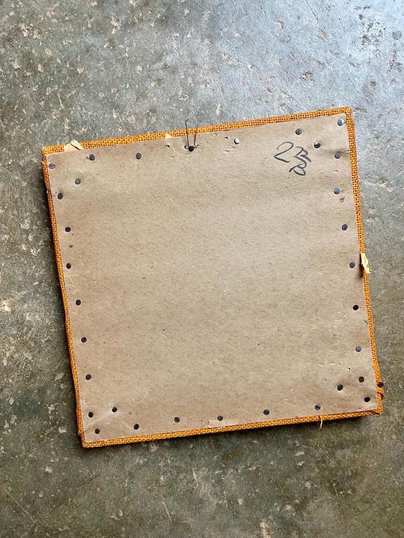 Pode incluir: A parte de tr&aacute;s de uma moldura de imagem quadrada, de cart&atilde;o castanho, com uma borda de tecido amarelo. A moldura &eacute; fixada com tachas pretas e tem o n&uacute;mero "238" escrito a tinta preta no canto superior direito.