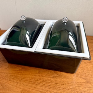 May include: A rectangular black serving container featuring two white-rimmed compartments, each topped with a dark green, dome-shaped glass lid. Each lid is finished with a small, clear, spherical knob handle for easy lifting and access.