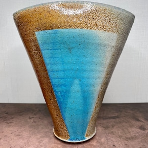 May include: A ceramic vase with a wide, flared opening and a narrow base. The vase is decorated with geometric shapes in shades of brown, blue, and white.