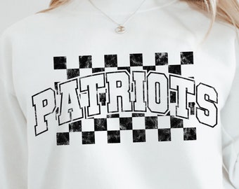 Op de afbeelding: Witte trui met een zwart-wit geruit ontwerp en het woord "PATRIOTS" in een zwart-wit vintage lettertype.