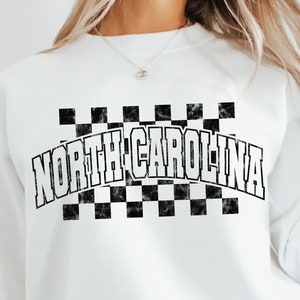 May include: White sweatshirt with a black and white checkered design and the text "NORTH CAROLINA" in a vintage style font.