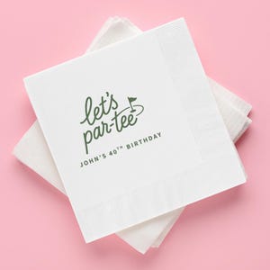 May include: A stack of white paper napkins featuring a green printed design. The text reads "let's par-tee" with a small golf flag icon, followed by the text "JOHN'S 40TH BIRTHDAY" in a simple sans-serif font. The napkins have a textured border.