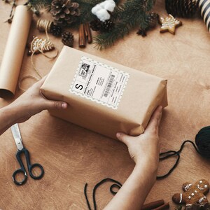 Hands holding a Christmas gift with a North Pole delivery sticker. Customizable design includes recipient name, address, and delivery method options like chimney or magic key.