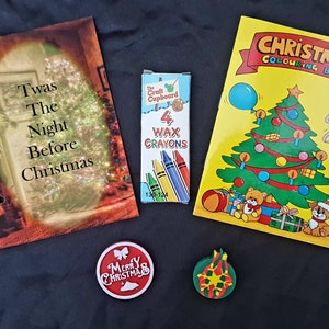 May include: A Christmas-themed gift set with a book titled "Twas The Night Before Christmas", a coloring book with a Christmas tree and a teddy bear, a box of four wax crayons, a red ornament with the text "Merry Christmas", and a green ornament with a snowflake design.