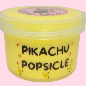 Op de afbeelding: Een gele slime in een doorzichtige plastic container met een geel deksel. De container heeft een label met de tekst "PIKACHU POPSICLE" met een Pikachu-personage erop.