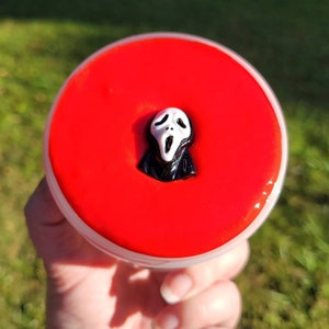 May include: A red slime with a black and white Ghostface mask charm inside a clear container.