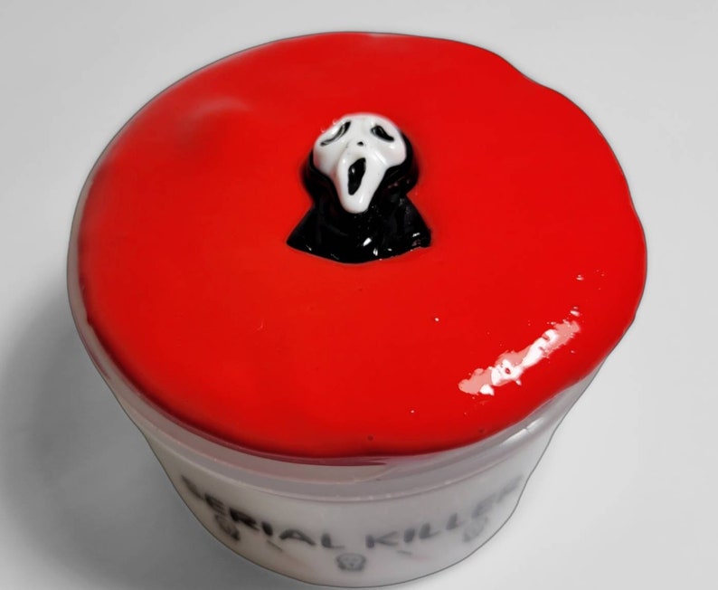 May include: Red slime with a white ghost mask on top in a clear plastic container with the words "Serial Killer" written on the bottom.