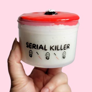 May include: A white container with a red lid and the text "SERIAL KILLER" printed on the front. The container has three black and white ghost face masks and knives printed on the front.
