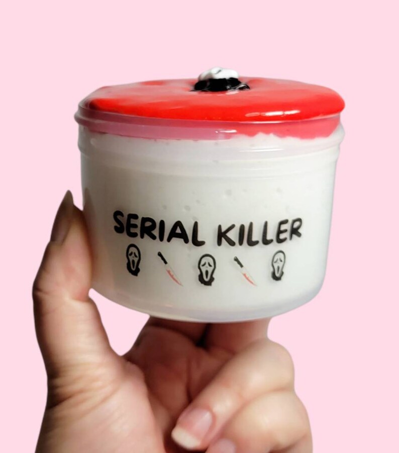 May include: A white container with a red lid and the text "SERIAL KILLER" printed on the front. The container has three black and white ghost face masks and knives printed on the front.