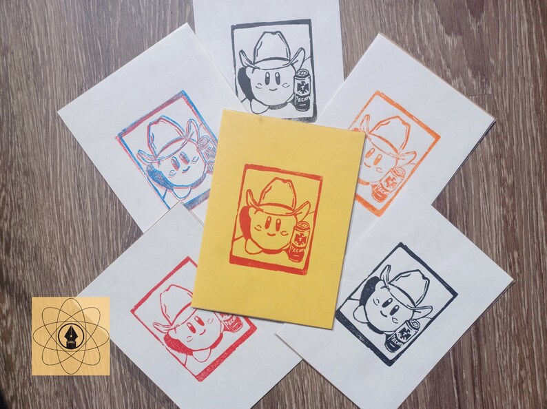 May include: A collection of linocut prints featuring a cartoon character wearing a cowboy hat and holding a can of soda. The prints are in various colors, including red, blue, orange, and black, on white and yellow paper.
